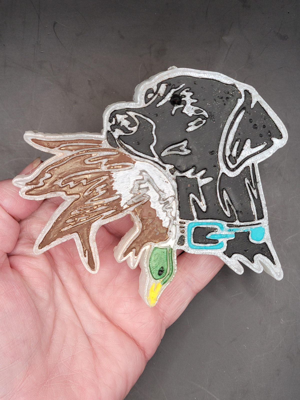Hand holding the black Lab and duck freshie with brown and white feather details.