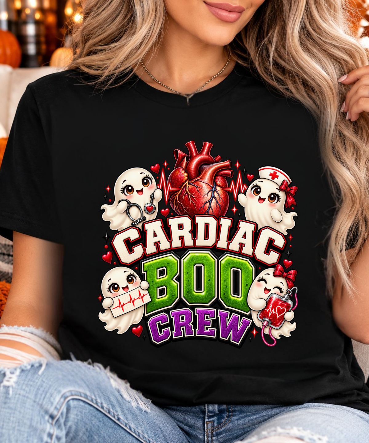 Blonde model wearing black Cardiac Boo Crew Halloween nurse T-shirt with cute medical ghosts, red anatomical heart and green and purple lettering.