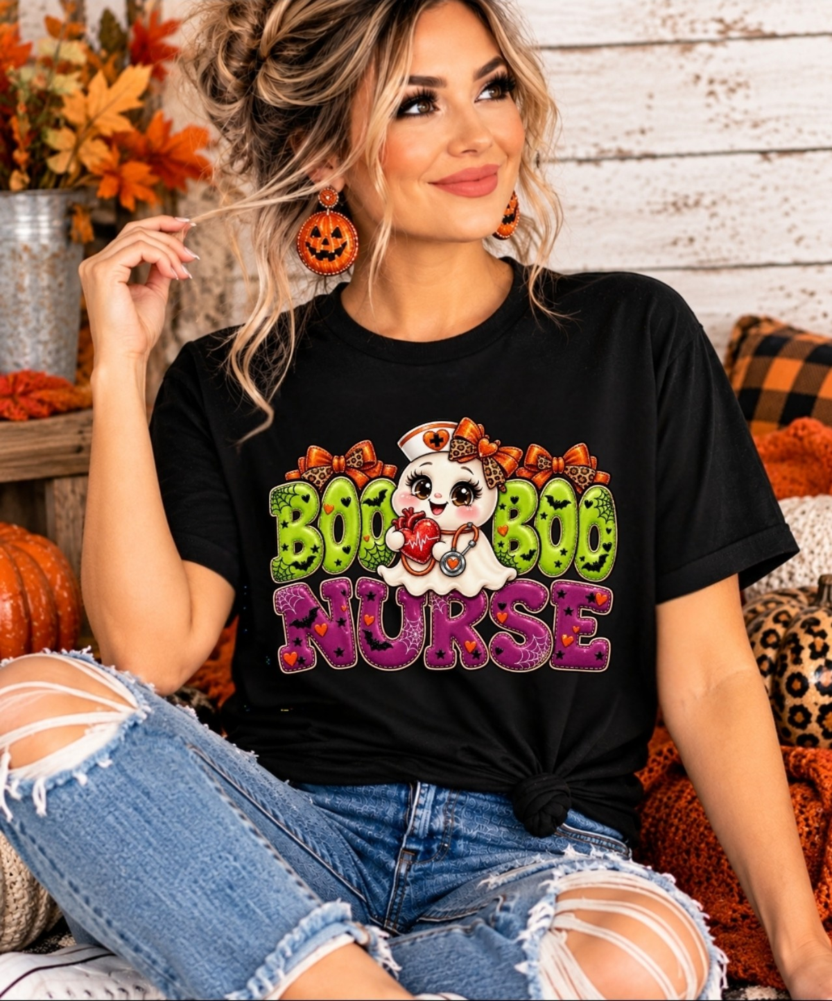 Seated model wearing a black Boo Boo Nurse graphic tee with lime green and purple Halloween lettering, paired with distressed jeans.