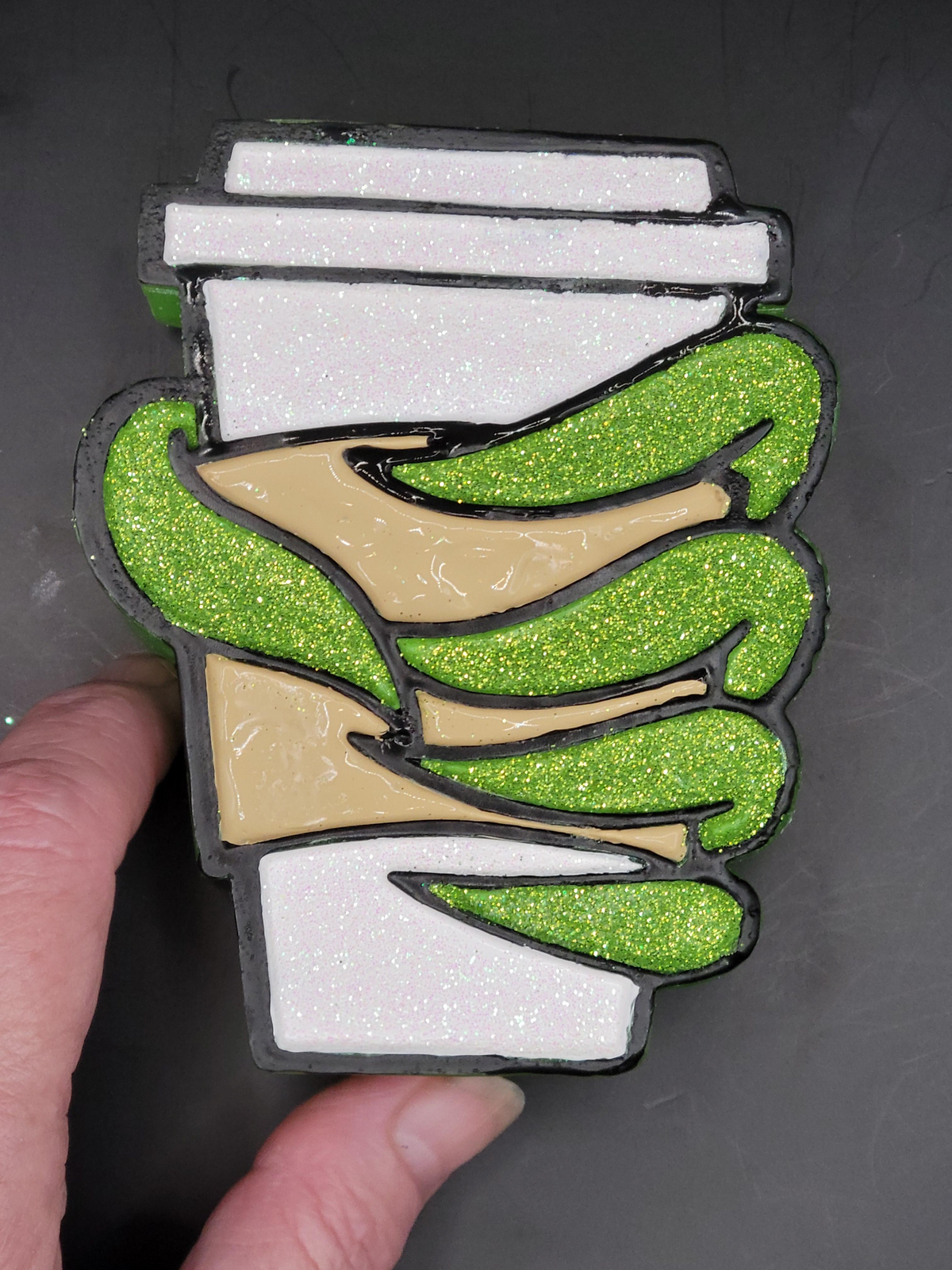 Hand holding the green glitter coffee cup freshie to show its relative size.