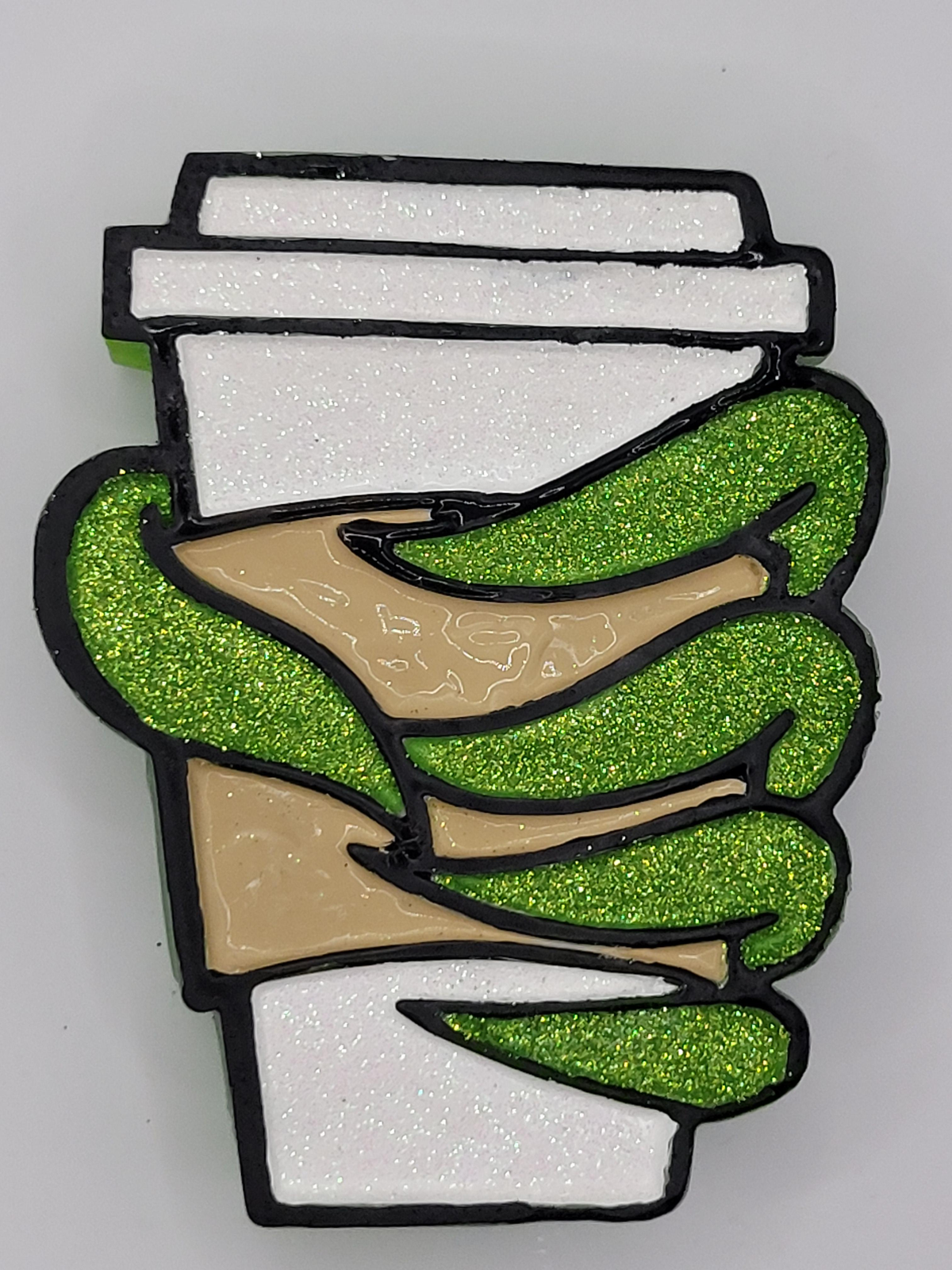 Green glitter hand with pointed nails wrapped around a white glitter coffee cup with a tan sleeve and black outlines.