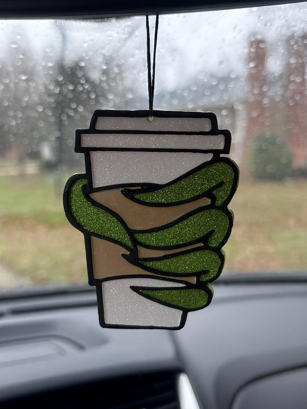 Green hand coffee cup freshie suspended by a black cord inside a vehicle.