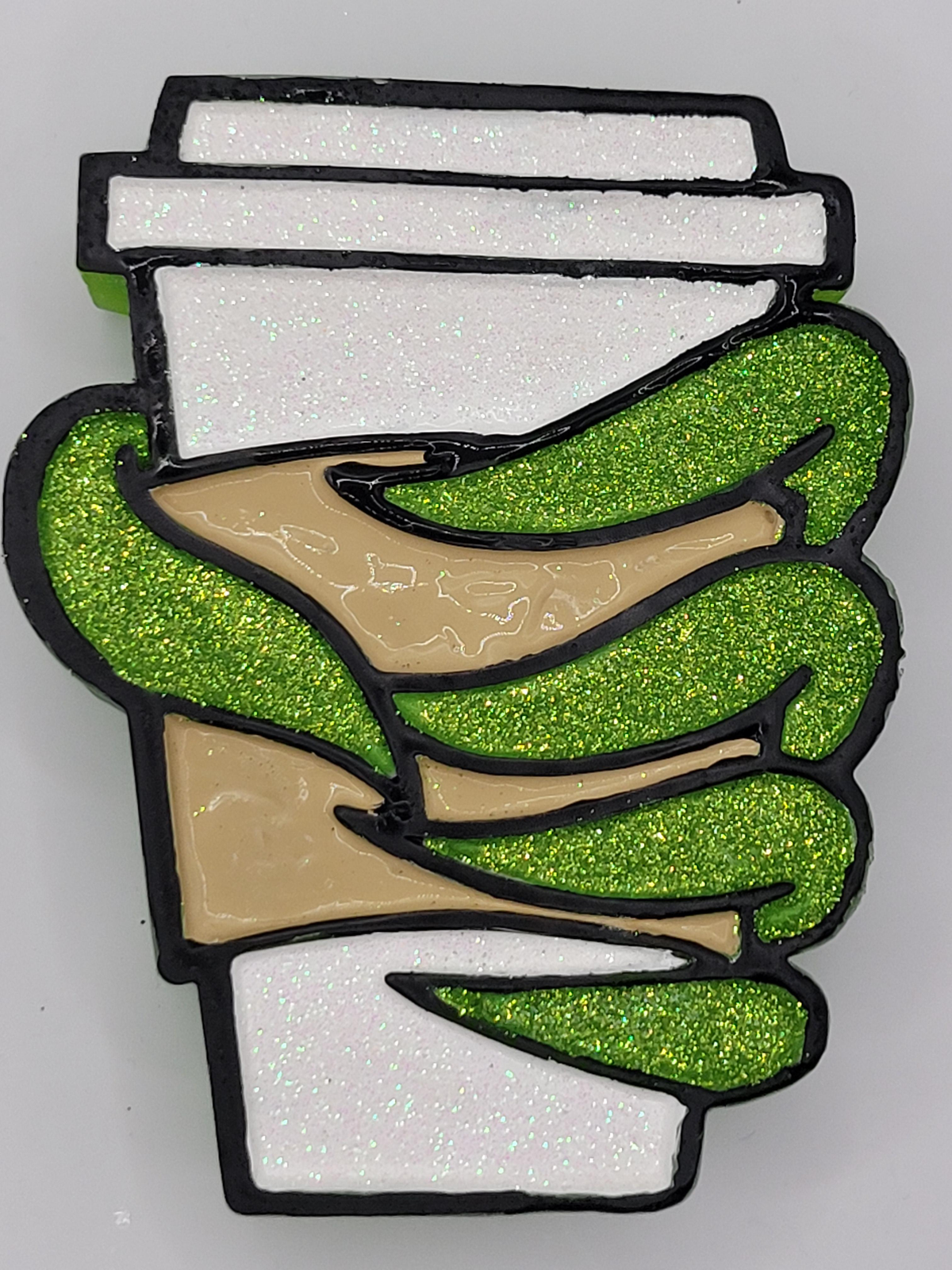 Close-up of green glitter fingers wrapped around a white glitter cup with a tan sleeve.
