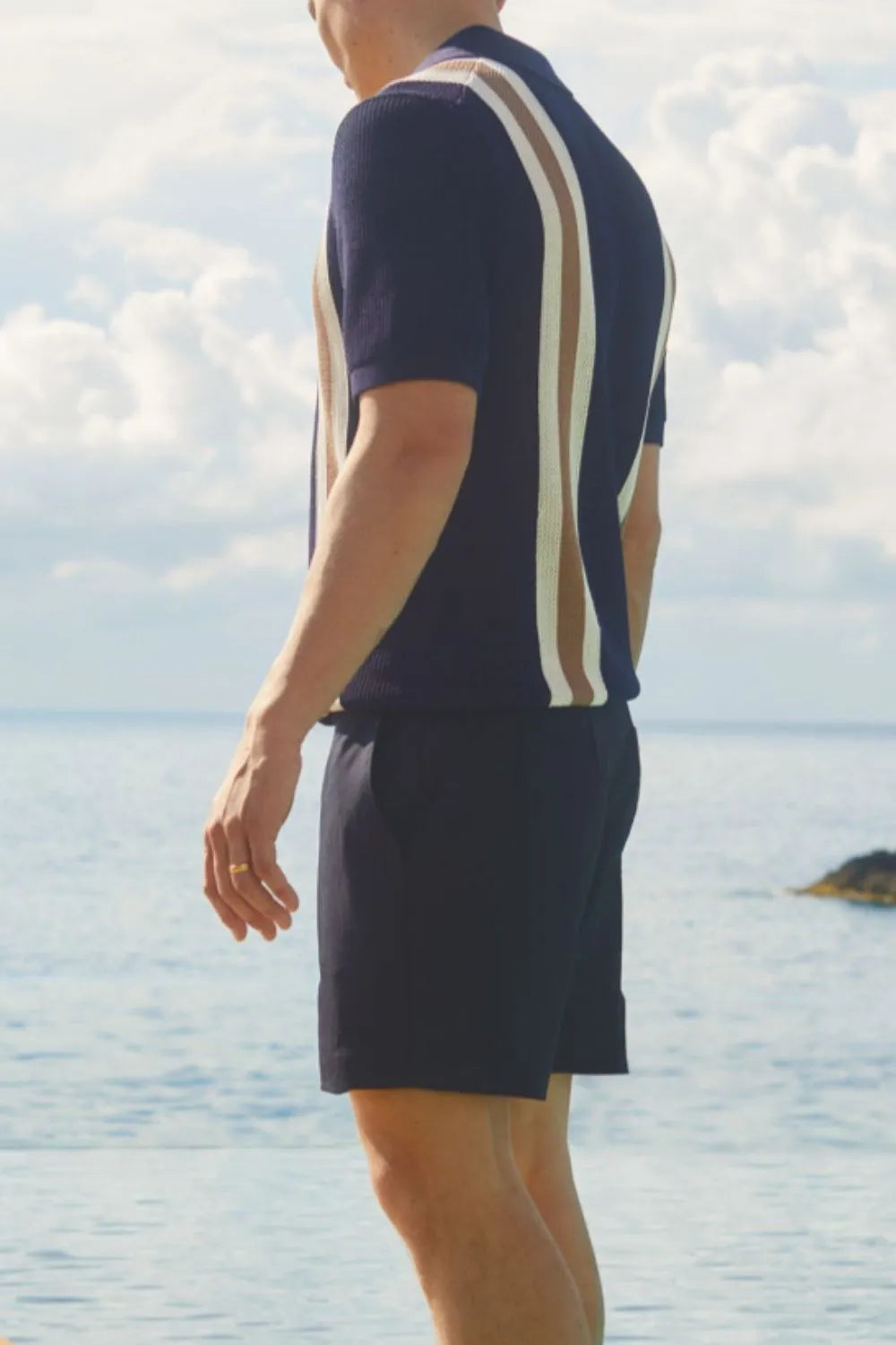 Man wearing a navy short sleeve button-down shirt with contrast vertical stripes, back and side view