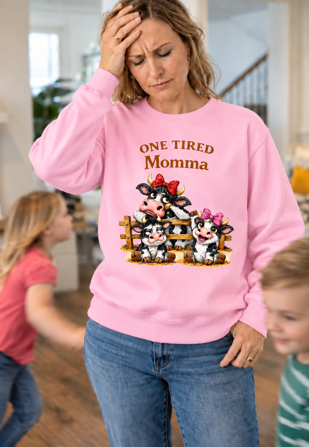 Woman wearing a pink Gildan crewneck sweatshirt with One Tired Momma cow graphic