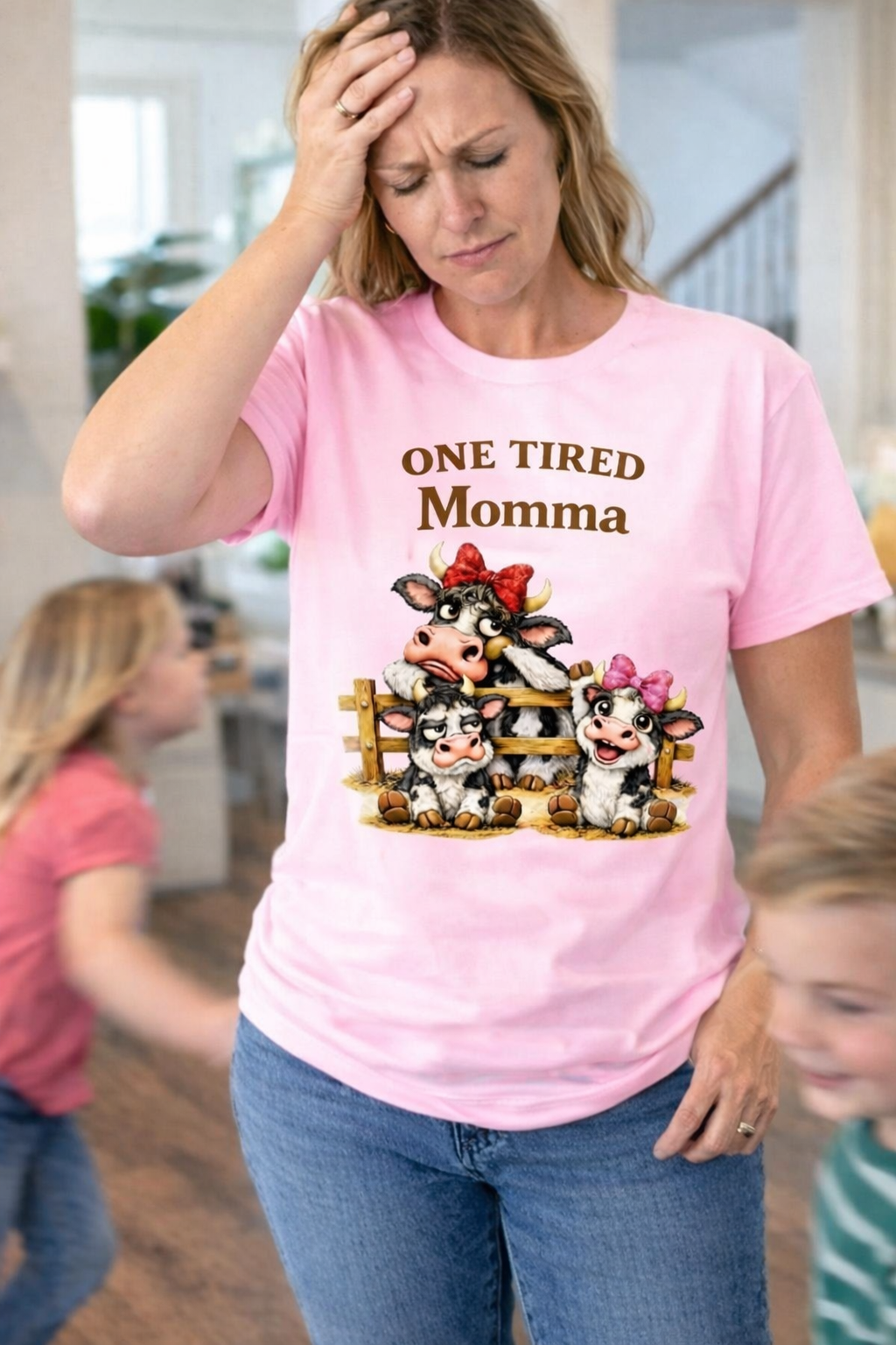 Woman wearing a pink T-shirt with One Tired Momma cow graphic in a home setting