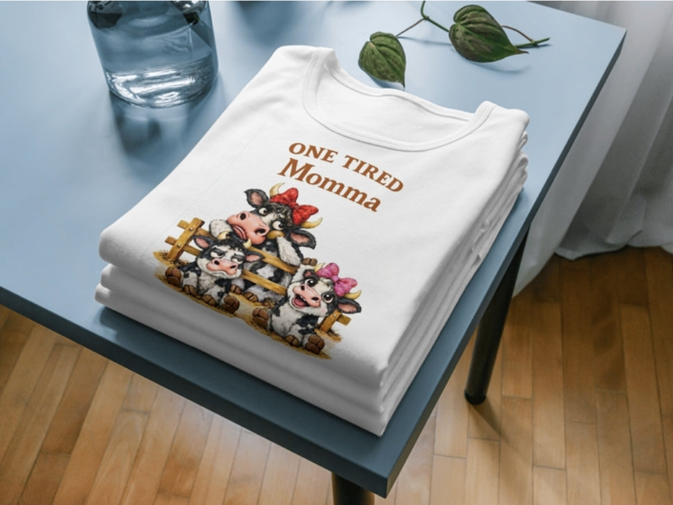 Woman wearing a white Gildan crewneck sweatshirt with One Tired Momma cow graphic