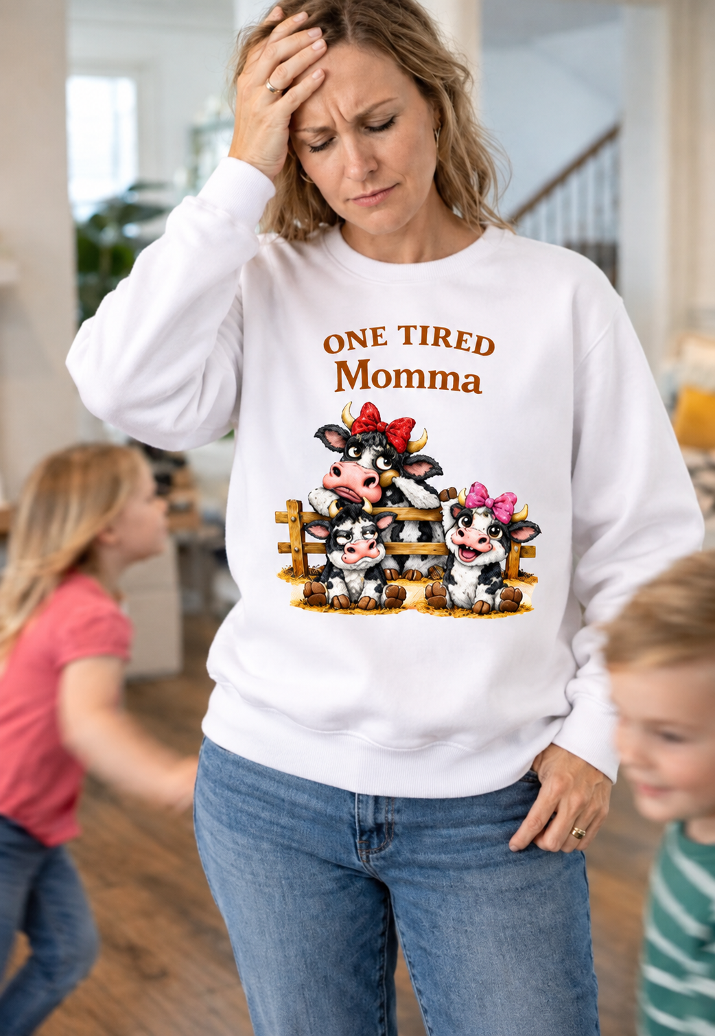 Woman wearing a pink Gildan crewneck sweatshirt with One Tired Momma cow graphic