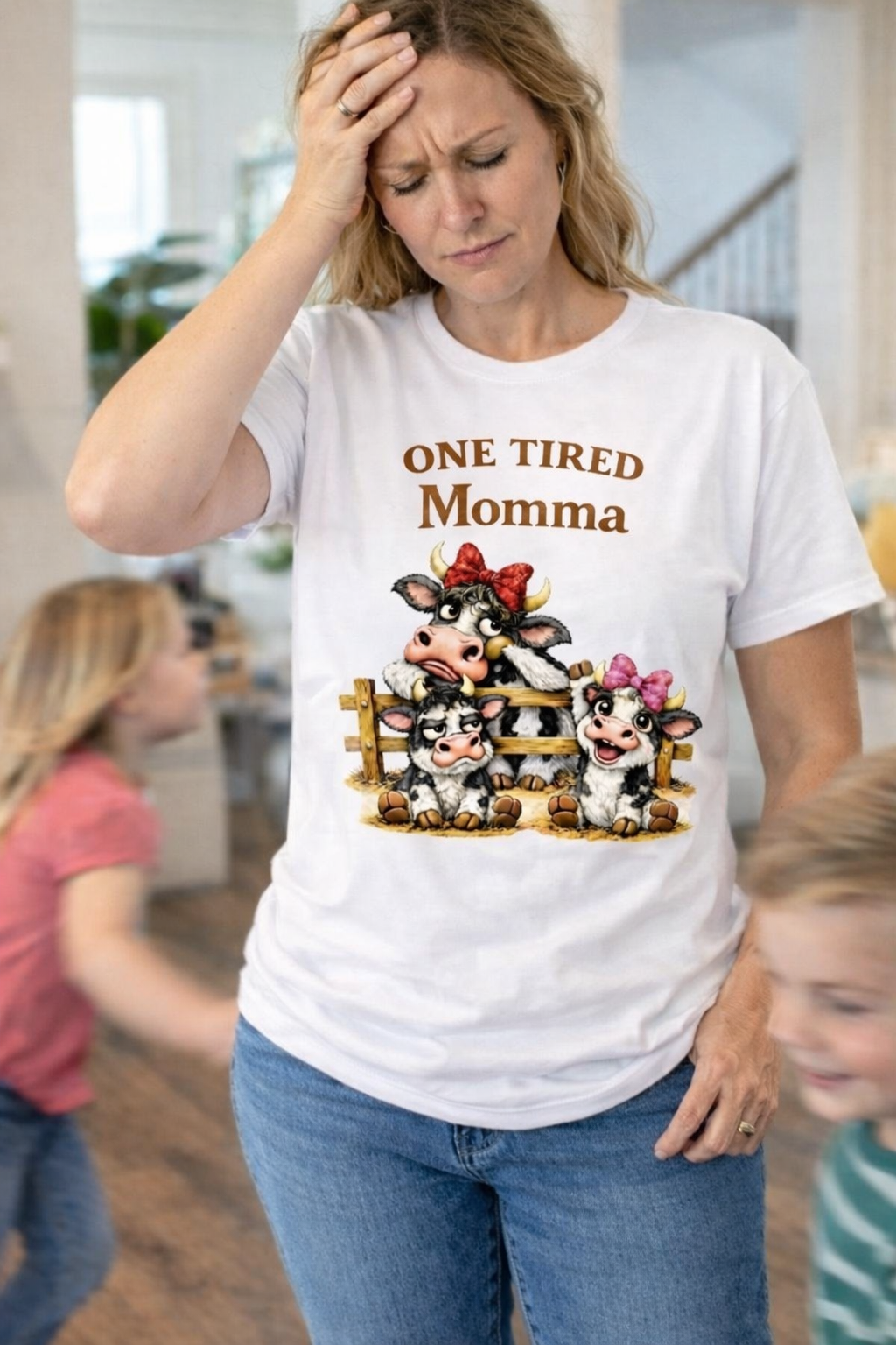 Woman wearing a white T-shirt with One Tired Momma cow graphic in a home setting