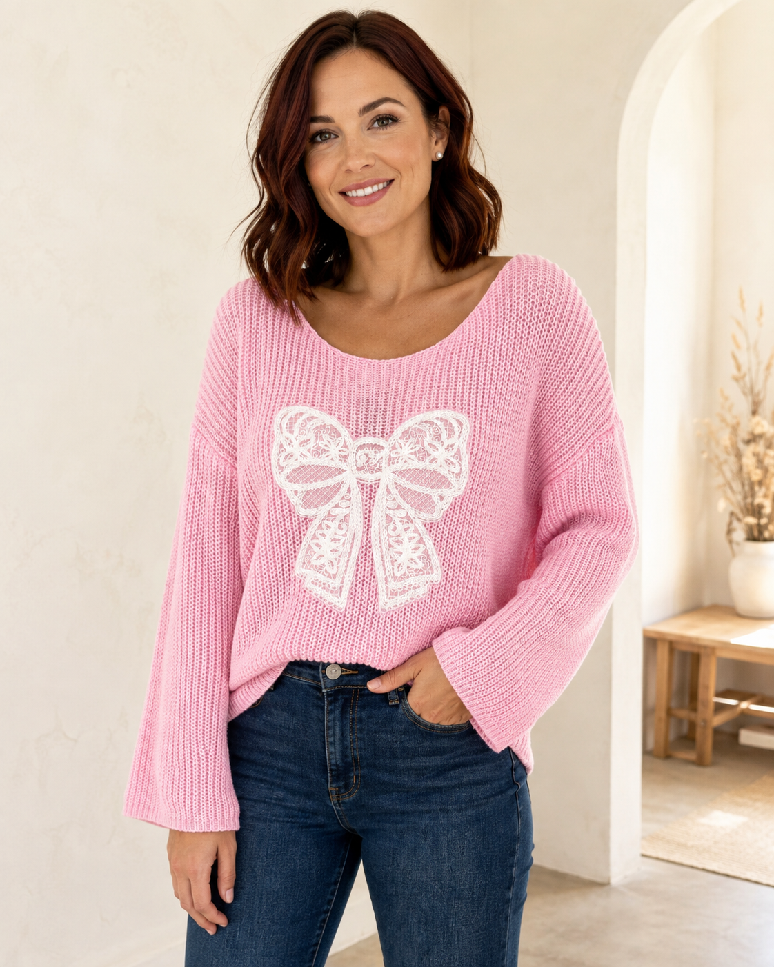 Woman modeling a pink open-knit sweater with a white lace bow and bell sleeves