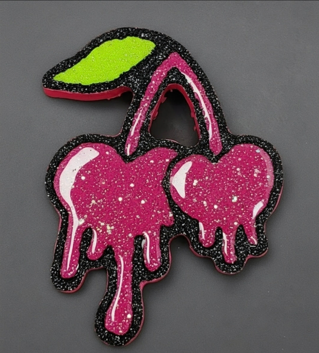 Close-up of pink dripping cherry car freshie with black glitter outline, green leaf and hand-painted white highlights.