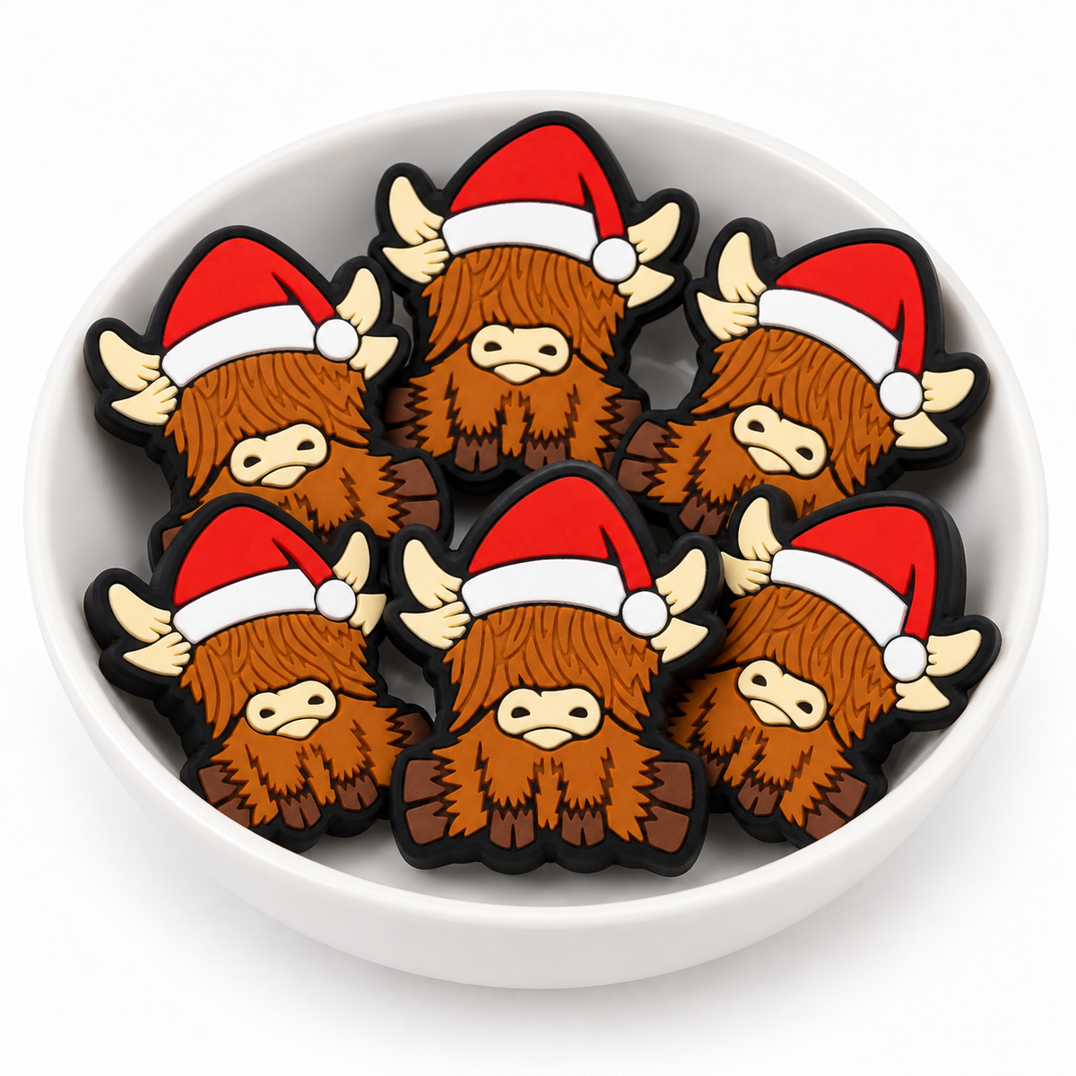 Six Christmas Highland cow focal beads arranged in a white bowl, showing Santa hats and detailed brown hair.